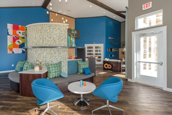 Infinity at Centerville Crossing Modern lounge with blue chairs, colorful pillows, mosaic-tiled wall, and large windows letting in natural light.