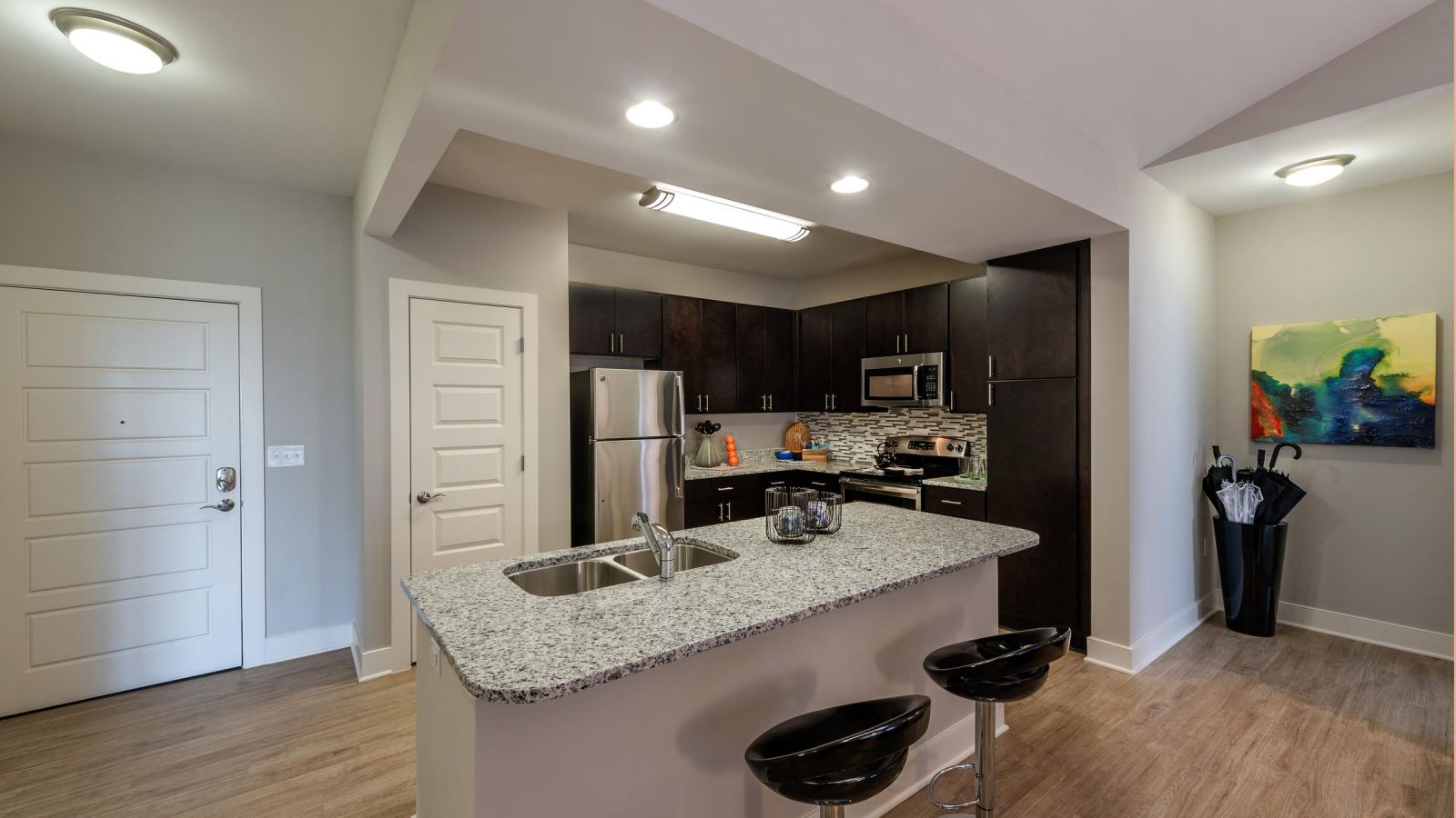 Modern kitchen and living area with white cabinets, stainless steel appliances, and a large island. Cozy seating area with a sofa and rug in the background. Bright and inviting atmosphere.
