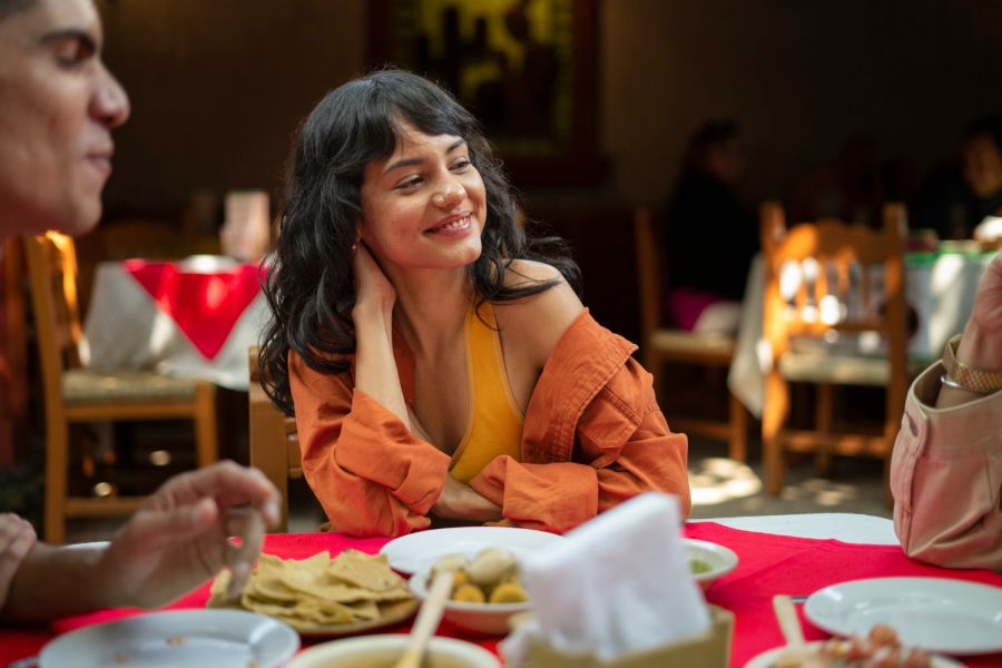 Infinity at Centerville Crossing Woman smiling at a table with friends, surrounded by food in a warmly lit restaurant.
