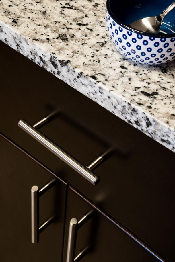 Infinity Crossings Apartments Granite countertop, dark cabinets with silver handles, and a blue bowl with white dots and a spoon.