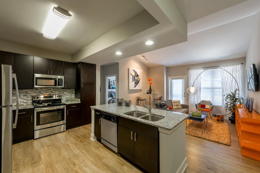 Infinity-at-Centerville-Crossing Modern kitchen with dark cabinets, stainless appliances, island, and view into a bright living room with orange accents.