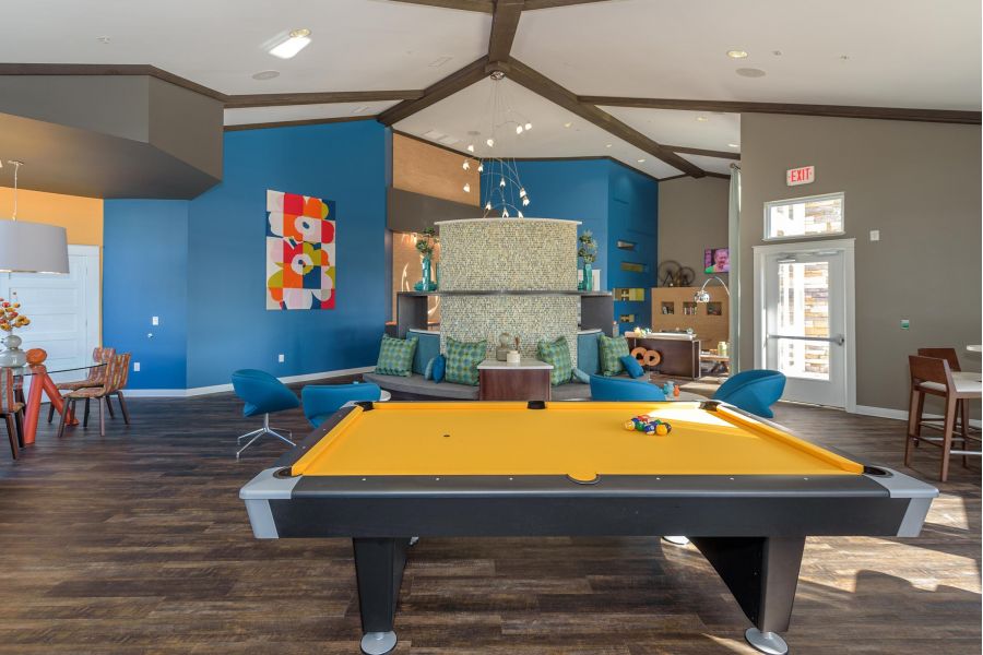 Infinity at Centerville Crossing Modern lounge with a yellow pool table, blue chairs, and colorful wall art in a bright, open room.
