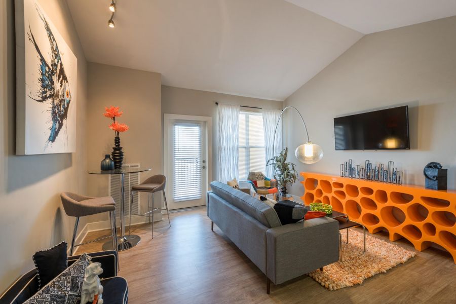 Infinity-at-Centerville-Crossing Modern living room with gray sofa, orange console, wall art, tall table with chairs, and large windows.