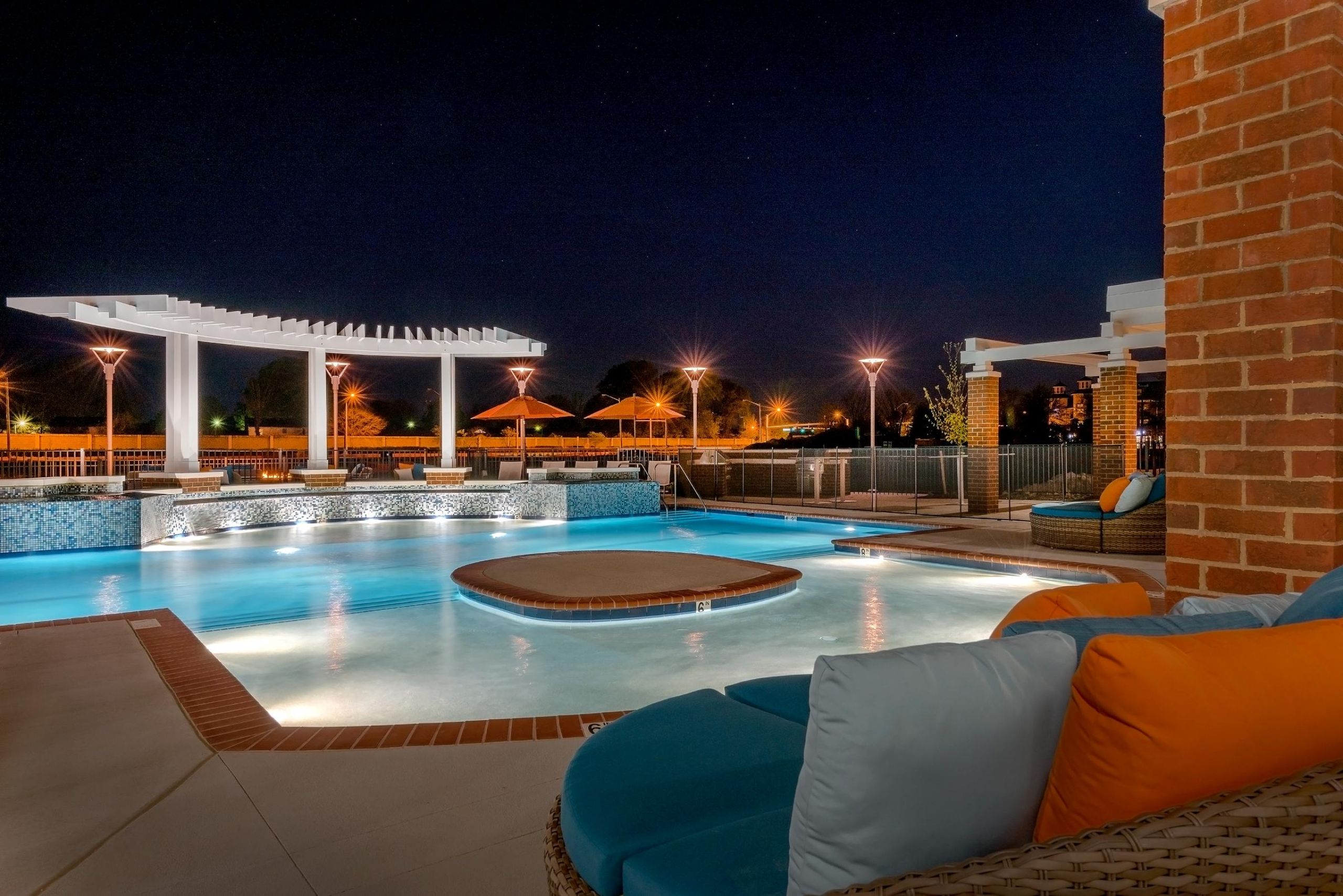 Infinity at Centerville Crossing Illuminated outdoor pool at night with lounge chairs, brick accents, and pergolas in the background.