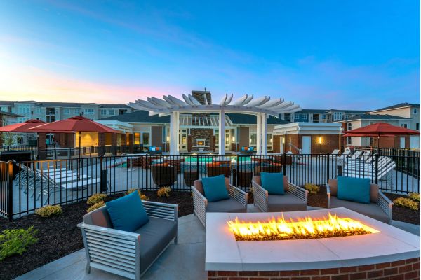 Infinity at Centerville Crossing Modern outdoor lounge with fire pit, pool, lounge chairs, and umbrellas at dusk in an apartment complex.