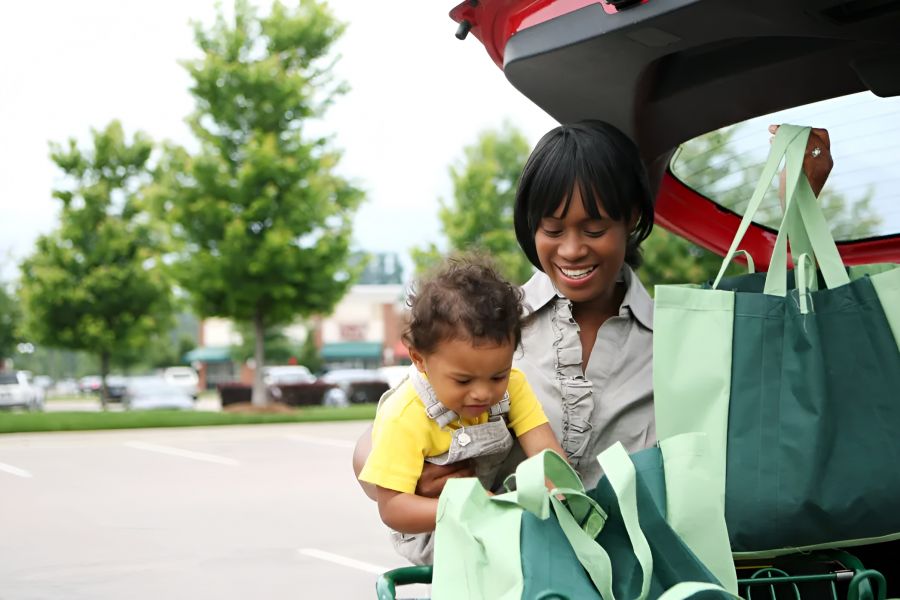 Attain on 5th apartment homes with A woman and young child unload green shopping bags from a car in a parking lot.
