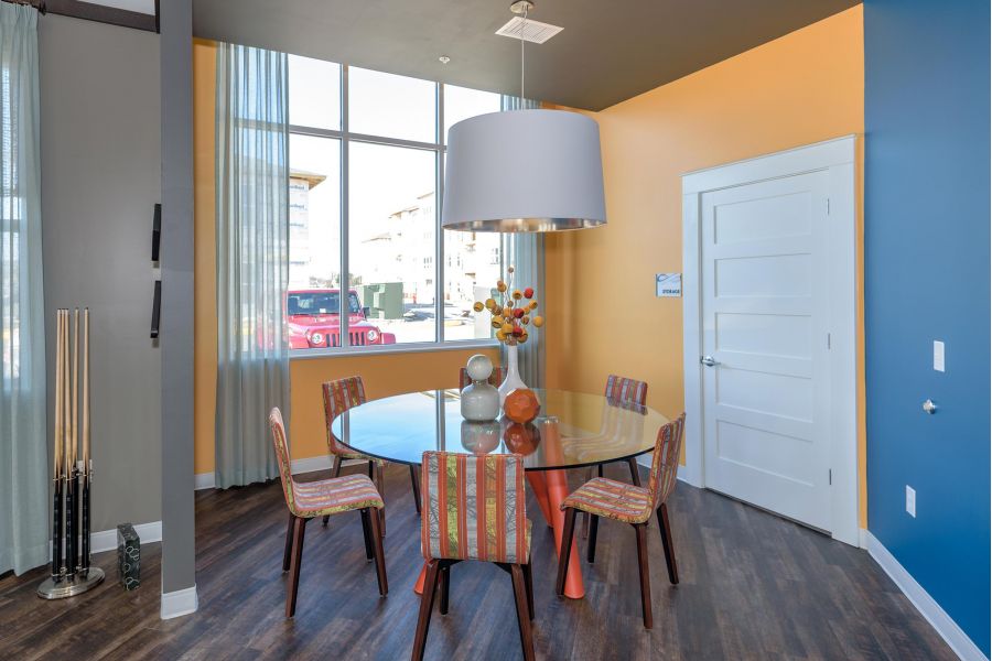 Infinity at Centerville Crossing Modern dining area with a round glass table, colorful chairs, large lamp, and bright yellow accent wall.