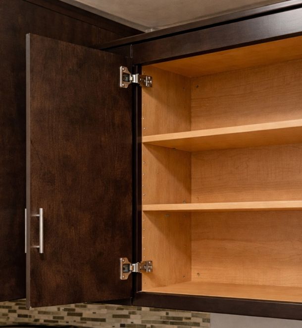 Infinity Crossings Apartments An empty wooden kitchen cabinet with dark brown doors and shelves, one door open.