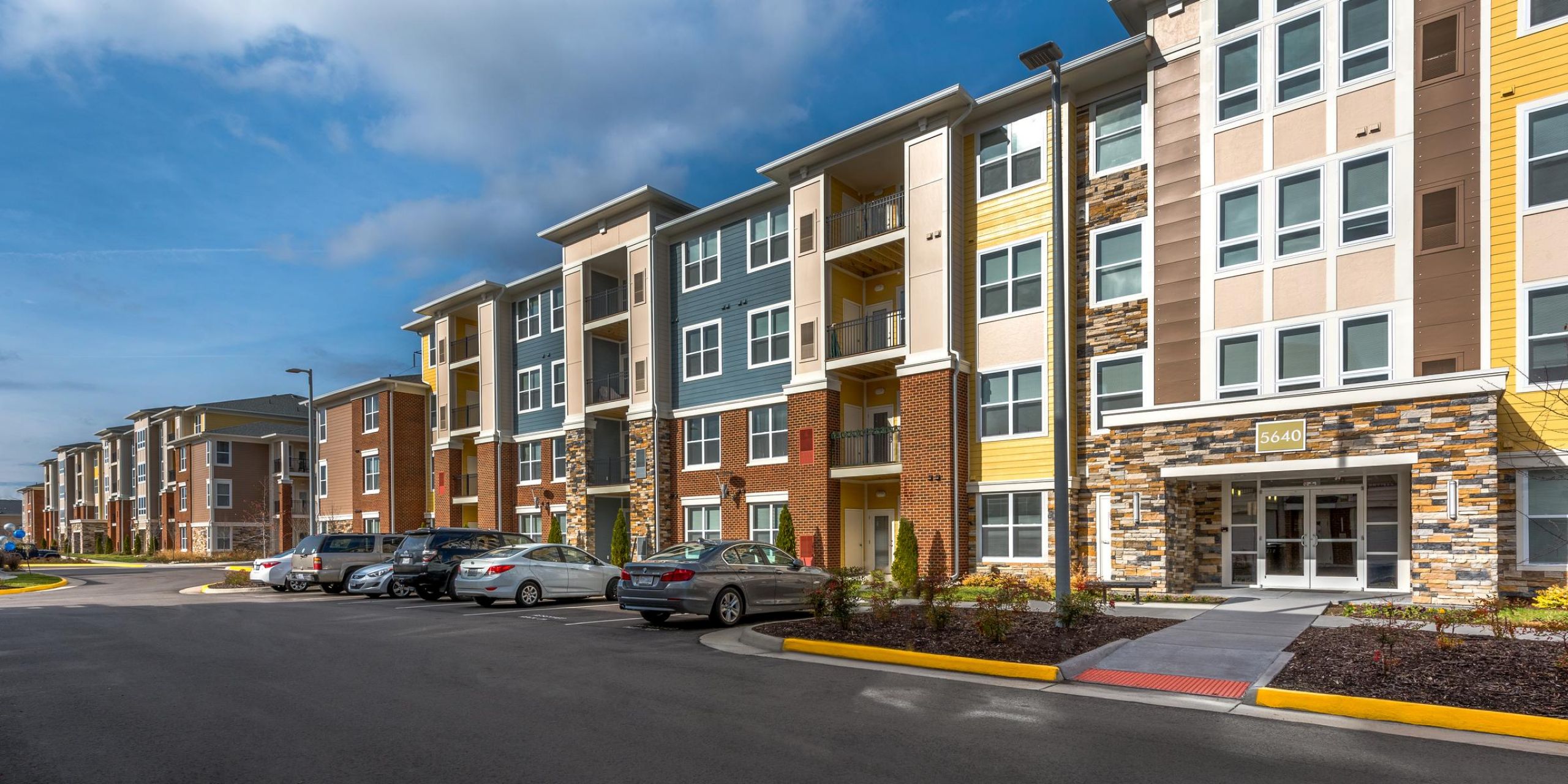 Infinity at Centerville Crossing Modern apartment complex with parked cars, multiple stories, and colorful exterior under a partly cloudy sky.