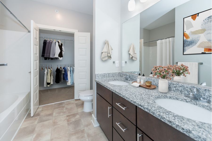 Infinity apartment homes with Modern bathroom with double sink vanity, flowers, and a view into a walk-in closet with hanging clothes.