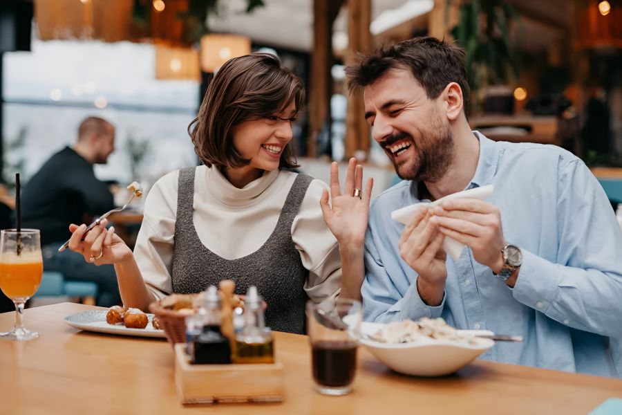 Infinity at Centerville Crossing A smiling couple enjoys a meal and laughs together at a restaurant table with drinks and food.