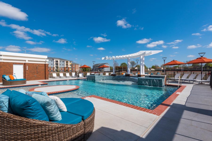 Infinity at Centerville Crossing Outdoor pool with lounge chairs, a pergola, and orange umbrellas under a clear blue sky.