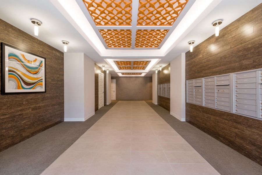 Infinity at Centerville Crossing Modern hallway with mailboxes on both sides, decorative ceiling panels, and abstract wall art.