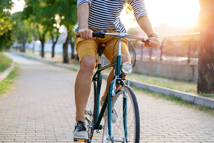 Infinity at Centerville Crossing Person riding a bicycle on a sunny paved path lined with trees, wearing a striped shirt and yellow shorts.